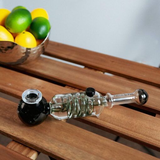 The Freeze Pipe with a black bowl sits on a wooden slatted table, while a metal bowl filled with lemons and limes is visible in the background.