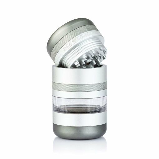 The RYOT GR8TR JAR BODY GRINDER features a silver and transparent cylindrical jar body, a clear central chamber, and a tilted top showing sharp metal teeth. It boasts a modern metallic design for efficient grinding.