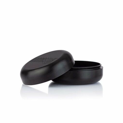 A round, black RYOT GR8TR JAR BODY GRINDER with its lid slightly open reveals an empty interior. The matte finish and subtle embossed lid text stand out elegantly against a white background.