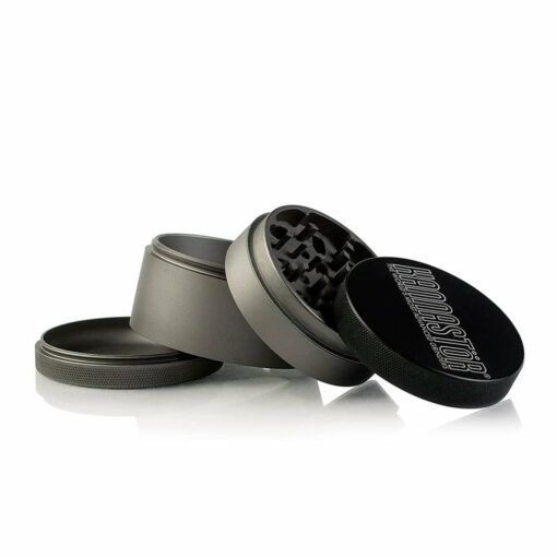 A four-piece metal herb grinder from the RYOT 4PC SOLID BODY GRINDERS line is displayed with its sections apart to reveal the interior grinding teeth and mesh screen, and features a black lid.