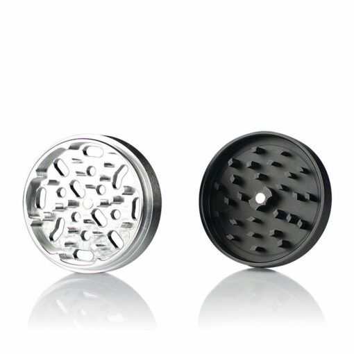 An open RYOT 4PC SOLID BODY GRINDER is shown with two separate parts: a silver piece featuring sharp teeth and a black one with angled blades, reflecting the classic craftsmanship of premium RYOT grinders.