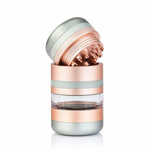 The RYOT GR8TR JAR BODY GRINDER features a metallic pink and silver design with a transparent middle, shown with the top unscrewed to reveal sharp teeth. Its sleek look stands out against a plain white background.
