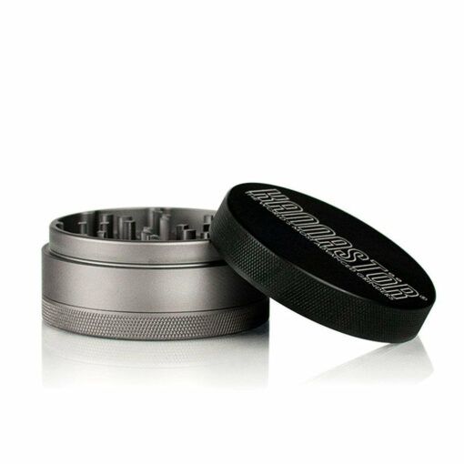 A metal herb grinder with a textured grip and an open black lid angled aside reveals sharp teeth inside. The bold RYOT logo stands out—perfect for fans of 4PC grinders like the RYOT 4PC JAR BODY GRINDERS.