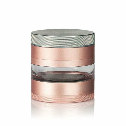 A metallic rose gold and silver RYOT 4PC JAR BODY GRINDER with a clear middle section, designed in a cylindrical shape, is displayed on a white background.
