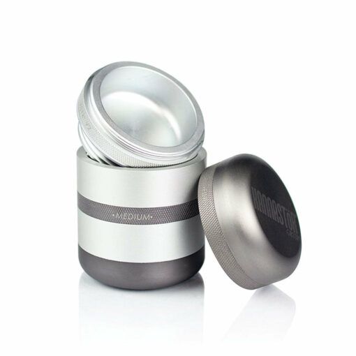 The RYOT GR8TR SOLID BODY GRINDER, a metallic grinder with a brushed silver and gray finish, features three detachable parts including a transparent lid and a screw-on top labeled HAMMERSTONE, displayed against a white background.