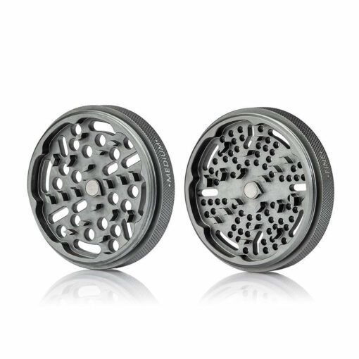 Two RYOT GR8TR SOLID BODY GRINDER pieces sit side by side, showcasing sharp teeth and grinding holes with a textured grip edge, on a white reflective surface.