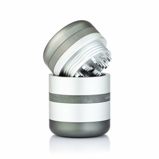 The RYOT GR8TR SOLID BODY GRINDER, a metallic cylindrical grinder with a textured grip, is displayed open with its top section tilted to reveal sharp grinding teeth inside, all set against a white background.