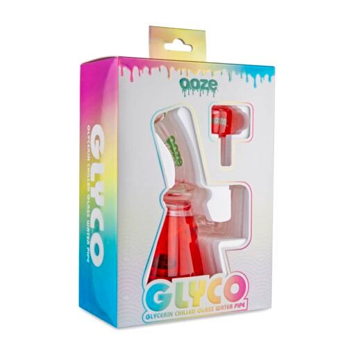 A boxed Ooze Glyco Bong Glycerin Chilled Glass Water Pipe with a red base is visible through a window in colorful packaging. The package also contains an accessory in its own compartment.