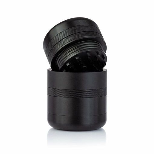 The RYOT GR8TR Solid Body Grinder in black metal features a textured grip and sharp grinding teeth, shown with the top half tilted and unscrewed on a white background.