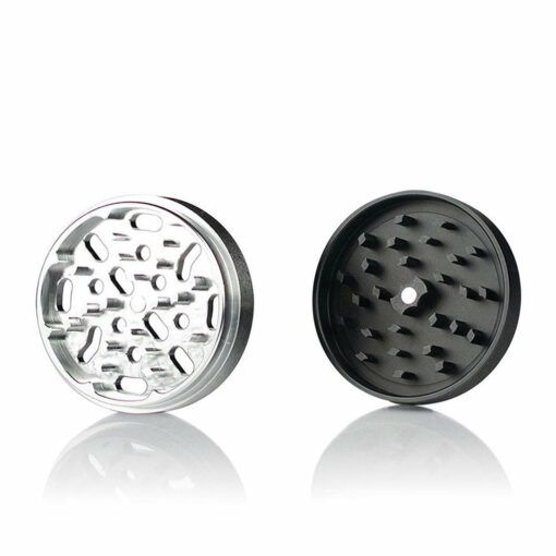 Two metal parts of the RYOT 4PC JAR BODY GRINDERS are shown: the left is silver with teeth and holes, and the right is black with sharp teeth, both set against a white background.