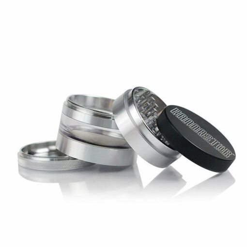 A disassembled RYOT 4PC JAR BODY GRINDER is shown, its silver and black parts arranged in a staggered row with the lid tilted to reveal grinding teeth and the embossed GRINDMASTER branding.