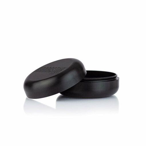 The RYOT GR8TR SOLID BODY GRINDER, a round black grinder with a matte finish and matching lid, sits partially open on a white background, showing its empty interior.