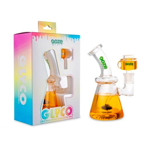 An Ooze Glyco Bong Glycerin Chilled Glass Water Pipe filled with orange liquid stands next to its colorful GLYCO-labeled box, which features a window revealing the chilled glass water pipe inside.