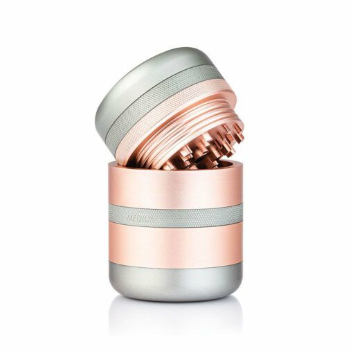 The RYOT GR8TR SOLID BODY GRINDER features rose gold and silver bands and is displayed open on a white background, showcasing its sharp grinding teeth inside.