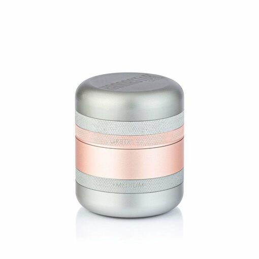 The RYOT GR8TR SOLID BODY GRINDER, a small cylindrical metal grinder with a matte silver finish and rose gold band around the middle, is shown against a plain white background.