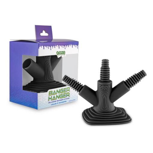 A black Ooze Banger Hanger Silicone Banger Stand with three angled prongs is shown next to its purple and white box, which has green accents and a clear window displaying the stand inside.