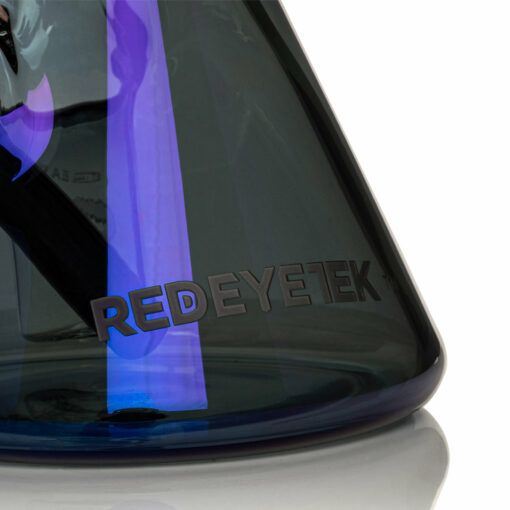 A close-up of the Gear Premium 12" Sidekick Beaker (Terminator Finish) Water Pipe with REDEYETEK etched on its side. The dark glass reflects blue and purple hues, and part of the interior glass tube is visible.