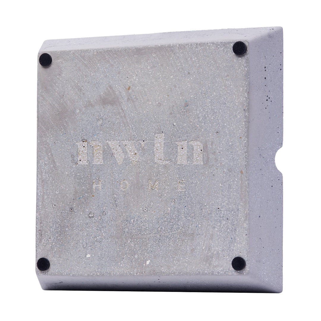 The NWTN Home Roseland Set Ashtray is a square concrete piece with rounded edges, four small black corner pads, "nwtn HOME" engraved on the front, and a curved indentation on the right edge.