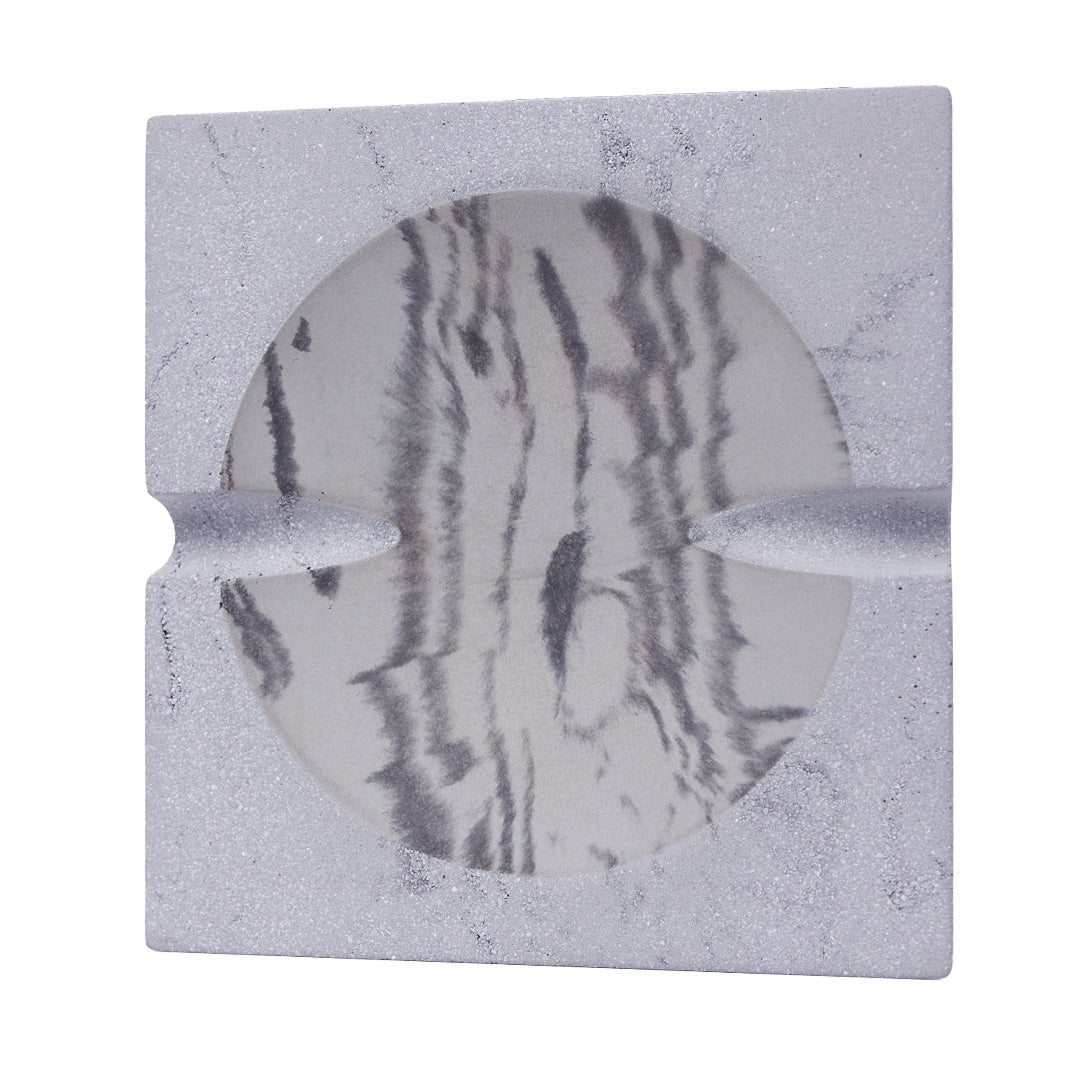 The NWTN Home Roseland Set Ashtray is a square, light gray ashtray with a textured finish, featuring a round marbled black and white inner surface and two grooves for cigarettes.