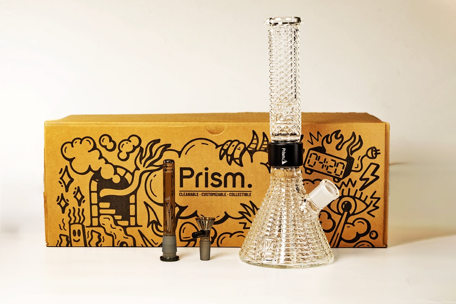 The Jane West x Prism Bong - Clear, featuring a textured design and removable parts, is shown in front of a brown box with playful black illustrations and "Prism" branding. Two metal components are displayed next to the bong.