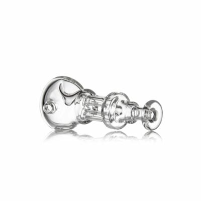 The MJ Arsenal Tetra, a clear glass pipe with a cylindrical, intricate design and decorative accents, rests on its side against a white background, highlighting its smooth and reflective surface.