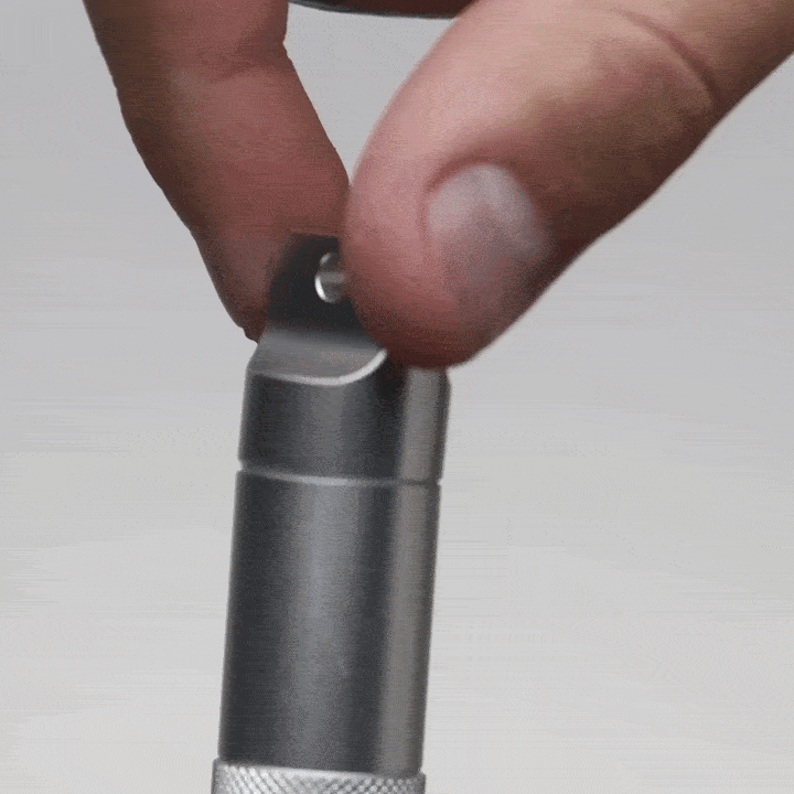 A hand twists open the cap of a metallic cylindrical container, resembling the Mj Arsenal Phoenix Baton, to reveal a set of small precision screwdrivers neatly nested inside.
