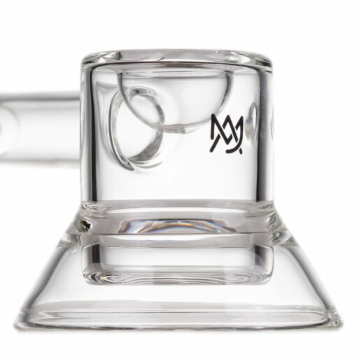 The MJ Arsenal Grotto Glass Pipe features clear glass with a flat base, angled sides, and a black MJ Arsenal logo resembling overlapping "M"s near the top. Designed for use as a dab rig or pipe.