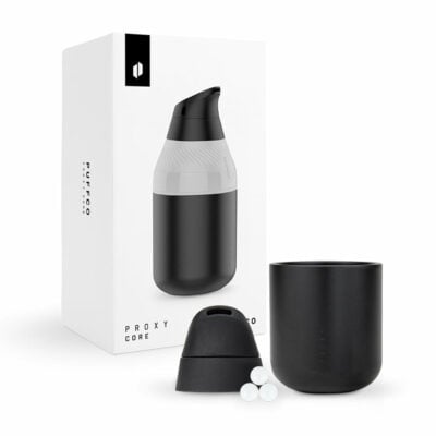 The Puffco Proxy Core, in sleek black, comes with a cup, lid, and three small white balls, displayed in front of its matching box showcasing the minimalist and modern design.