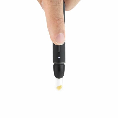 A hand holds the Puffco New Hot Knife, a black electronic device with a clear tip holding a yellowish substance, set against a white background.
