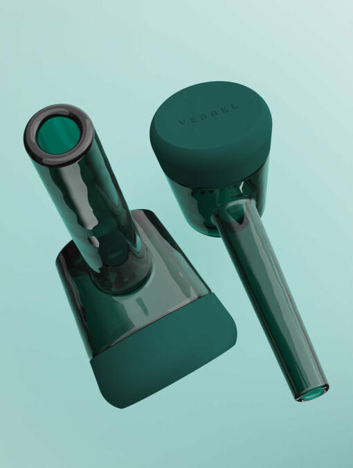 Two sleek, modern Forge [Emerald] glass containers with cylindrical shapes and rounded bases rest on a light teal background. One stands upright showing "VERSEL" on top; the other lies tilted, creating a stylish impression.