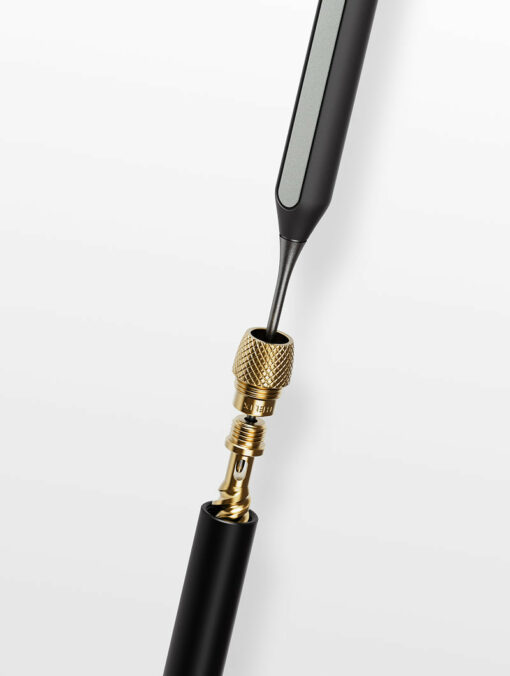 A close-up of the Care Kit’s gold valve core removal tool unscrewing a brass valve core from a black cylindrical bicycle tire valve against a white background.