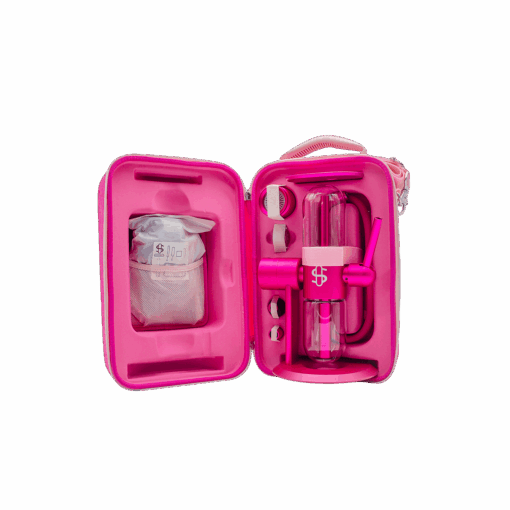 A bright pink case opens to reveal the Stündenglass Kompact Gravity Infuser - Pink, along with a grinder, lighter, and accessories in custom slots. A separate pouch with contents is secured on the case's left side.