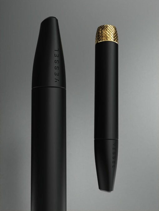 Two sleek Helix [Matte Black] pens are displayed on a gray background. Both are engraved with VESSEL; one is uncapped, and the other has a textured gold Helix cap.