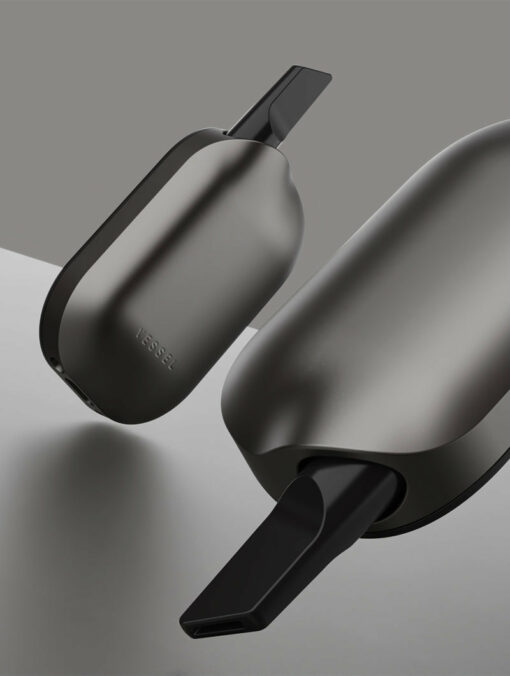 Two sleek Compass [Gunmetal] vape devices with black mouthpieces are displayed against a gray background—one in the foreground and one behind—highlighting their modern, minimalist design.