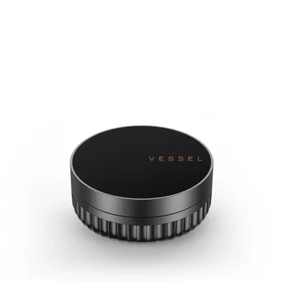 A black, round grinder with textured sides and copper VESSEL lettering on the lid sits on a white background—an ideal match for your Drift Case [Gunmetal].