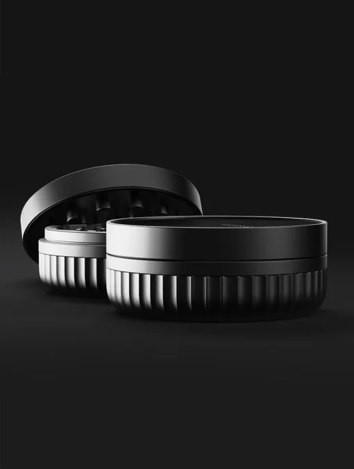 Two black, round Drift Case [Gunmetal] objects are on a dark background—one upright, the other open to display its sleek, ridged design and smooth top in stylish gunmetal tones.
