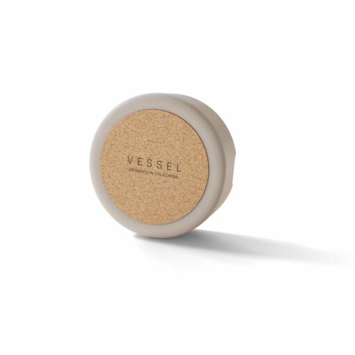 A round, beige Ember [Concrete] container with a cork lid featuring VESSEL and DESIGNED IN CALIFORNIA, set against a white background.