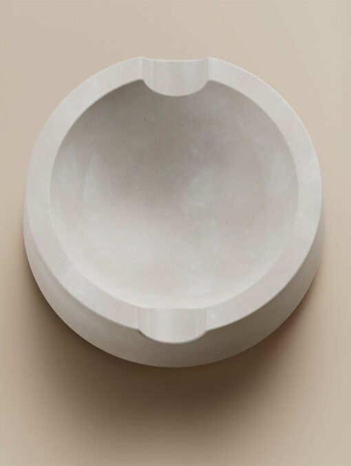 Ember [Concrete] is a round, white marble ashtray with two notches for cigarettes, displayed on a light beige surface, bringing warmth and style to any concrete setting.