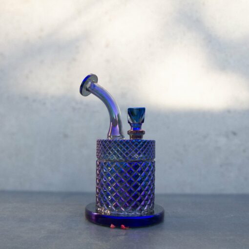 The Twenties Collection Water Pipe | Midnight, a small glass piece with fine patterns, a short curved neck, and a diamond-shaped bowl, rests on a flat surface against a plain light background.
