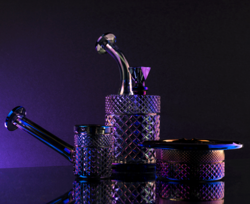 Three Twenties Collection Water Pipe | Midnight pieces are displayed on a reflective surface, bathed in purple and blue light against a dark background.