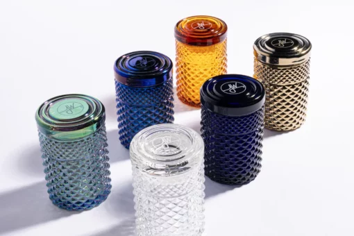 The Twenties Collection Jar | Mermaid set includes six cylindrical glass containers with textured diamond patterns in clear, blue, green, orange, and gold. Each jar has a matching round lid and evokes mermaid-inspired hues.