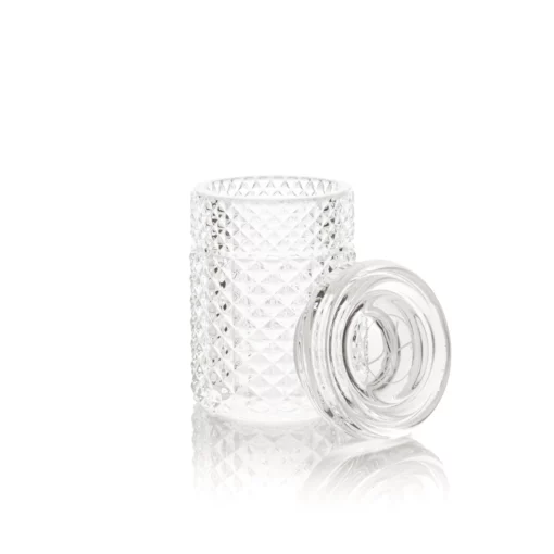 The Twenties Collection Jar | Clear features a diamond-patterned texture and sits on a reflective white surface, its round lid placed beside it to showcase the open jar’s vintage-inspired elegance.