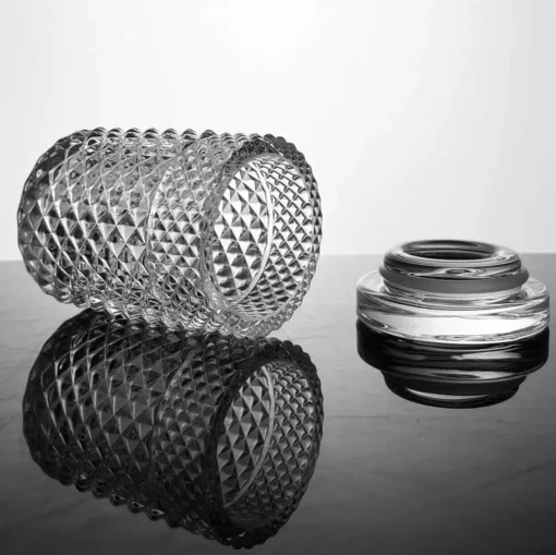 The Twenties Collection Jar | Clear tumbler rests on its side next to its smooth glass lid, both reflecting beautifully on a glossy black surface with striking contrasts of light and shadow.