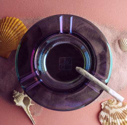 The Twenties Collection Ashtray | Mermaid, holding a rolled joint, sits on pink sand amid seashells. Blue and purple reflections play subtly on this decorative ashtray, viewed from above.