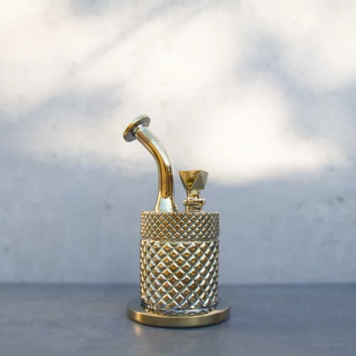 A gold Twenties Collection Water Pipe with a textured diamond pattern sits on a gray surface against a light, blurred background.