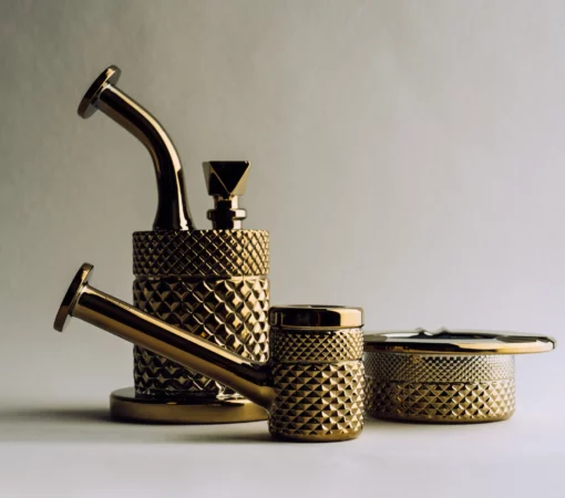 The Twenties Collection Water Pipe in gold features a textured, geometric pattern that reflects light elegantly against a plain background.
