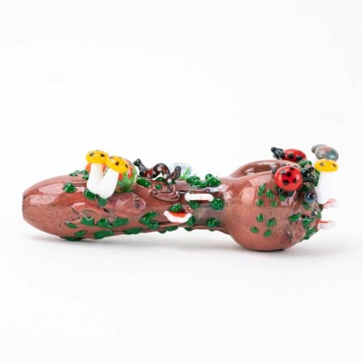 The Empire Glassworks Bug's Life Small Spoon Pipe features a brown log design adorned with colorful mushroom, ladybug, and insect details, as well as green moss-like accents. Shown on a white background.