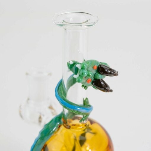 A close-up of the Empire Glassworks Dragon Sphere Mini-Tube shows its orange base and an intricate green glass dragon wrapped around the neck, with the dragon’s head and claws clearly visible against a plain white background.