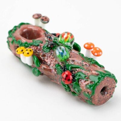The Empire Glassworks Mossy Log Dry Pipe is a glass piece crafted to resemble a log, featuring colorful mushrooms, ladybugs, green vines, and marbles for a lifelike natural look.