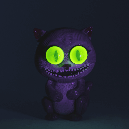 The Empire Glassworks Galacticat Dry Pipe features a cat with neon yellow-green eyes and a toothy grin, set against a dark background with purple and blue lighting—an out-of-this-world collectible piece.